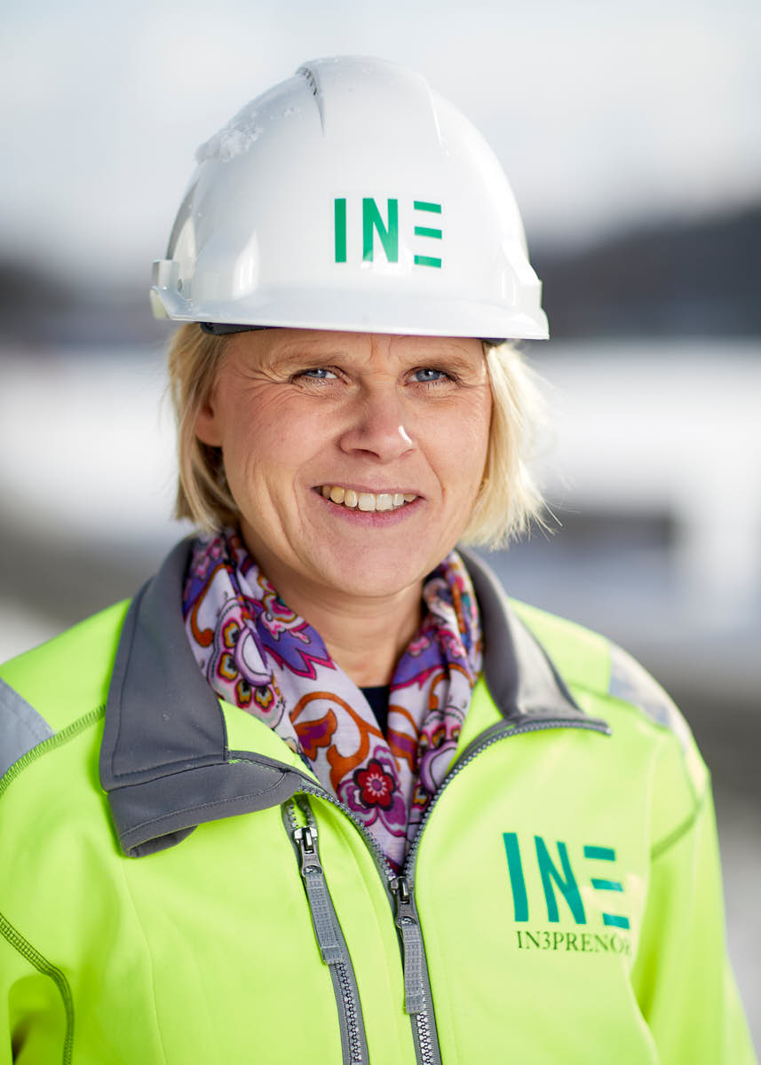 Porträtt av kvinnlig medelålders kvinna som ler och är medarbetare på Intreprenör, byggkläder och hjälm, utomhus på byggarbetsplats Uppsala.