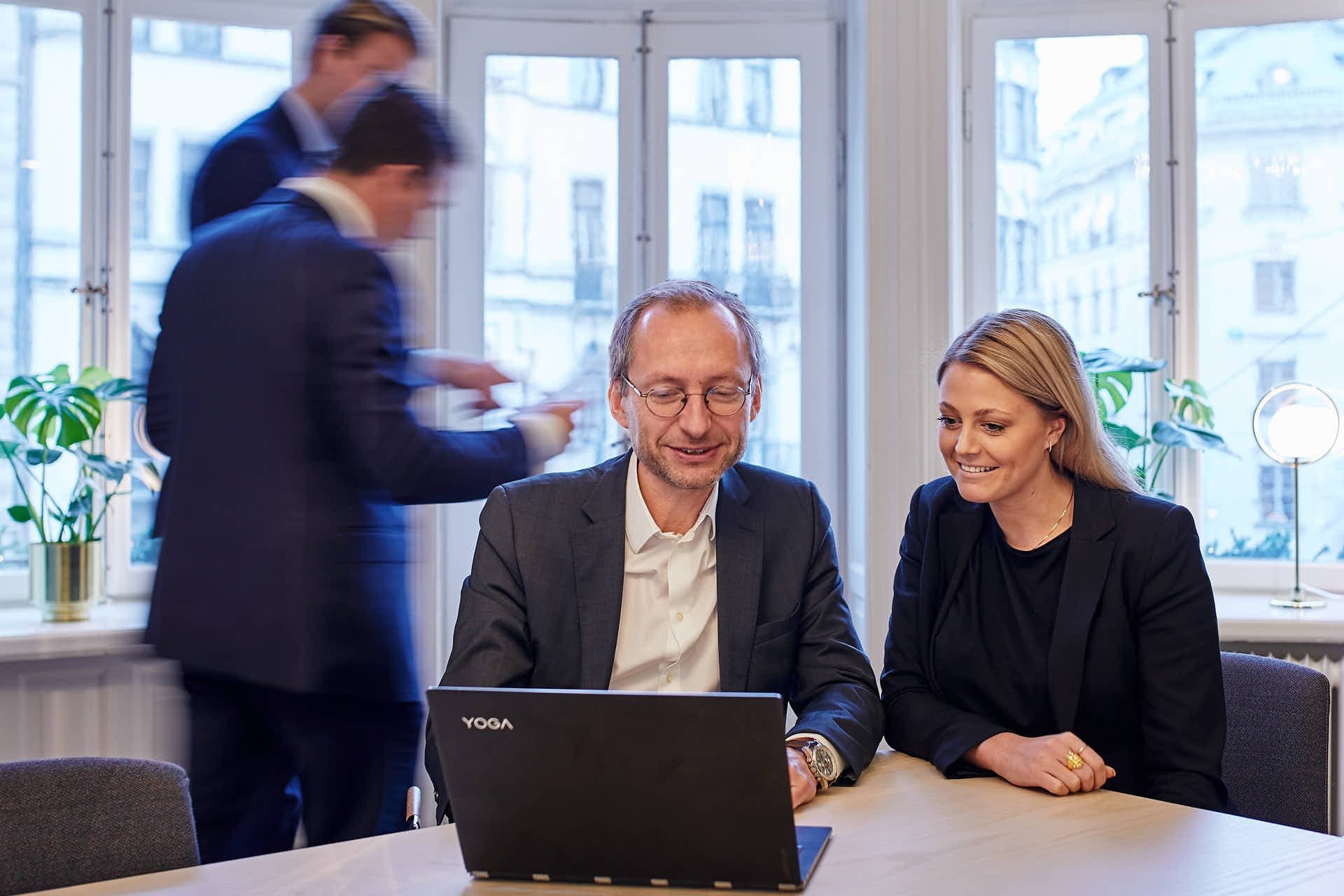 Investeringsbolag under möte, två personer tittar på dator och två personer går bakom dem i rörelseoskärpa, i Stockholm, foto Martin Ekwall.