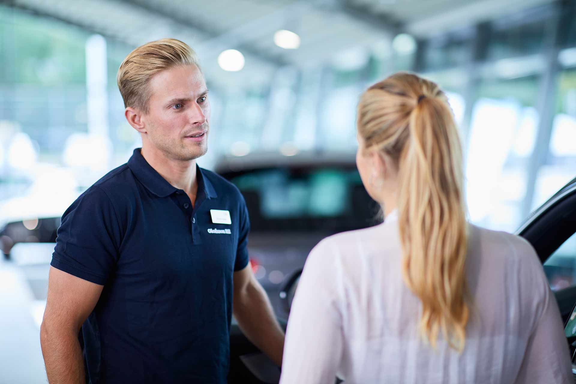 Säljare på Olofsson Bil (Bilia) pratar med kund vid bil i bilhallen, rådgivning inför köp. Foto Martin Ekwall.
