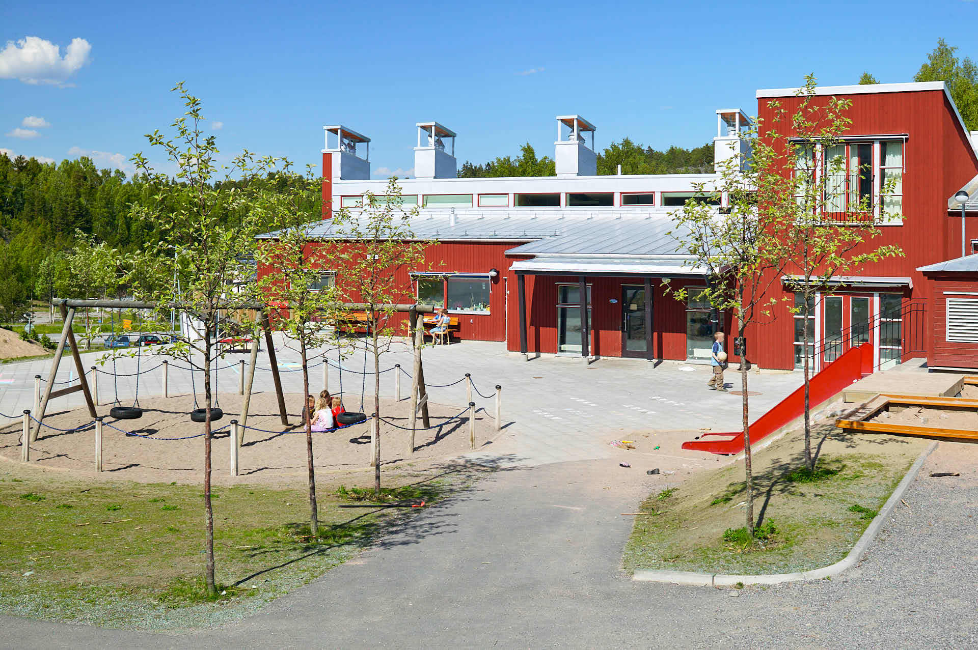 Skolgård med lekplats vid Brunns skola i Värmdö med gungor och rutschkana. Byggnaden ritades av White Arkitekter, foto av Martin Ekwall.