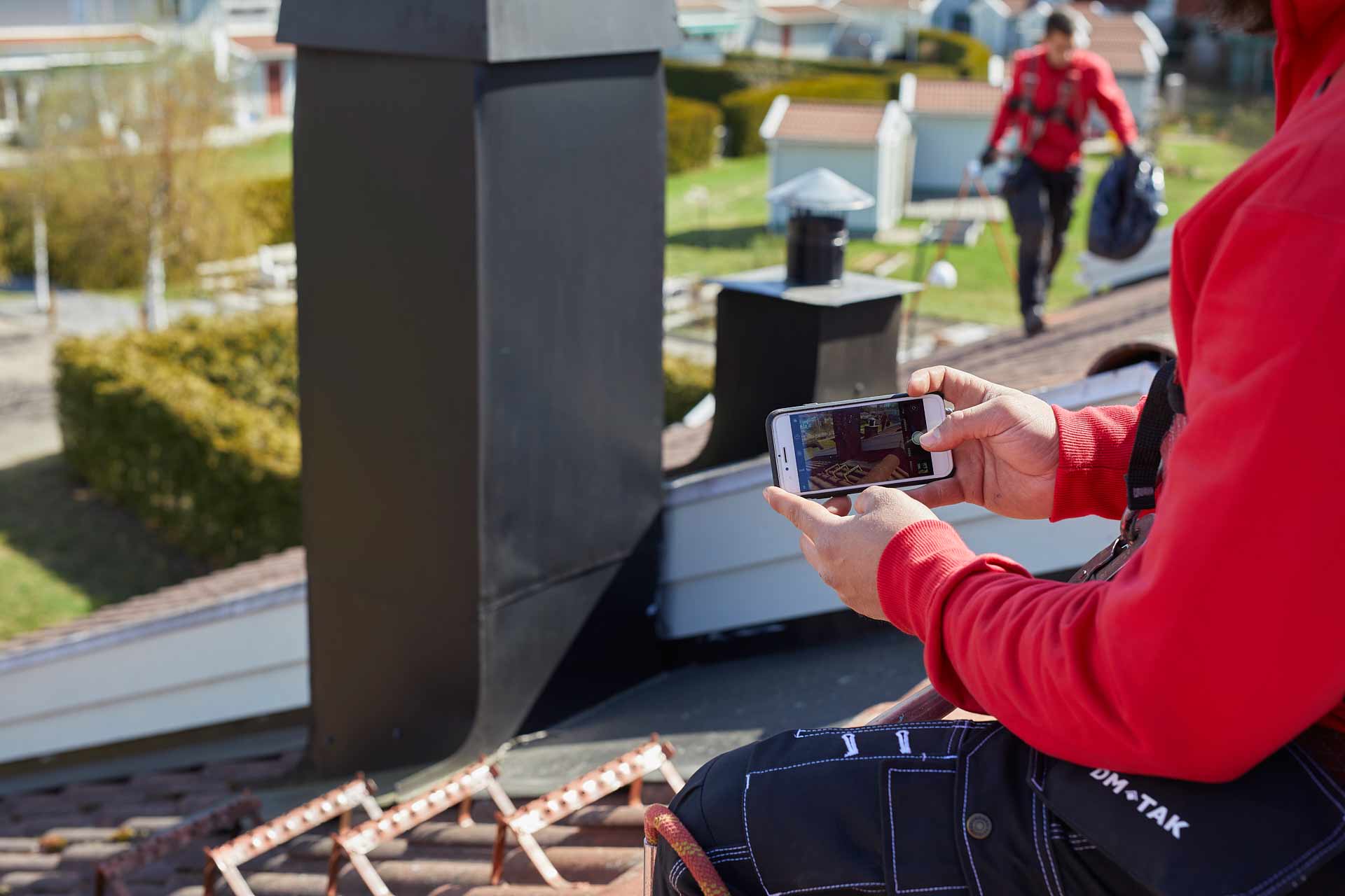 DM TAK takservice. Takarbetare fotograferar skorsten med mobil för dokumentation under takservice. Foto Martin Ekwall.