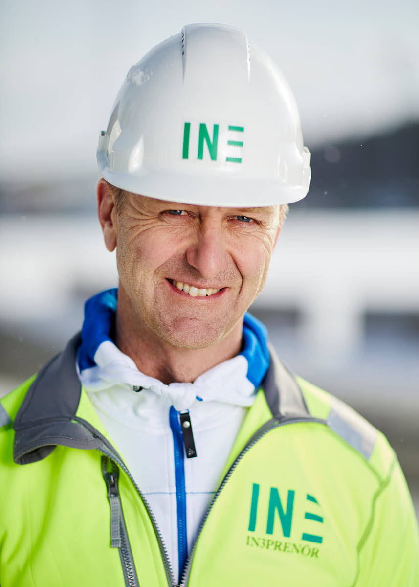 Porträtt av deleålders manlig medarbetare på Intreprenör, iförd i byggkläder och hjälm, utomhus på byggarbetsplats Uppsala.