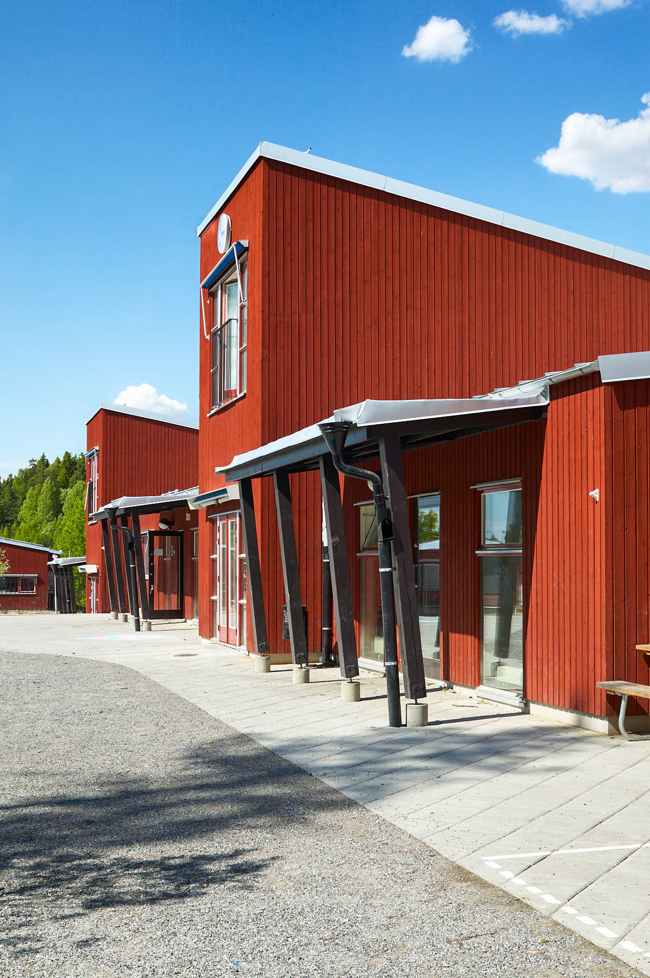 Fasad av Brunns skola i Holmen, Värmdö, sedd från sidan med skolgård. Faluröd träpanel, White Arkitekter ritade och arkitekturfoto av Martin Ekwall.