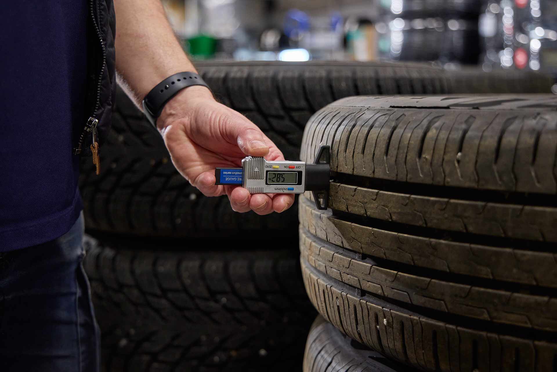 Medarbetare på Olofsson Bils däckcenter mäter däckdjup med digital mätare på staplade däck. Foto Martin Ekwall.