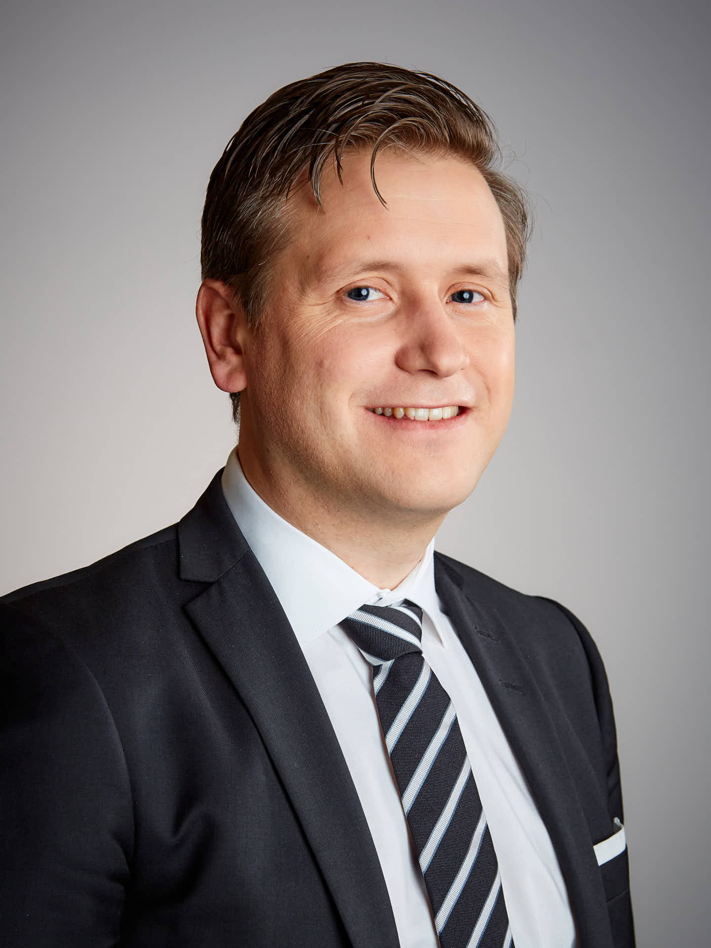 Ansiktsporträtt av man i svart kostym och svart-vitrandig slips mot grå bakgrund, Ramirents styrelse. Foto Martin Ekwall