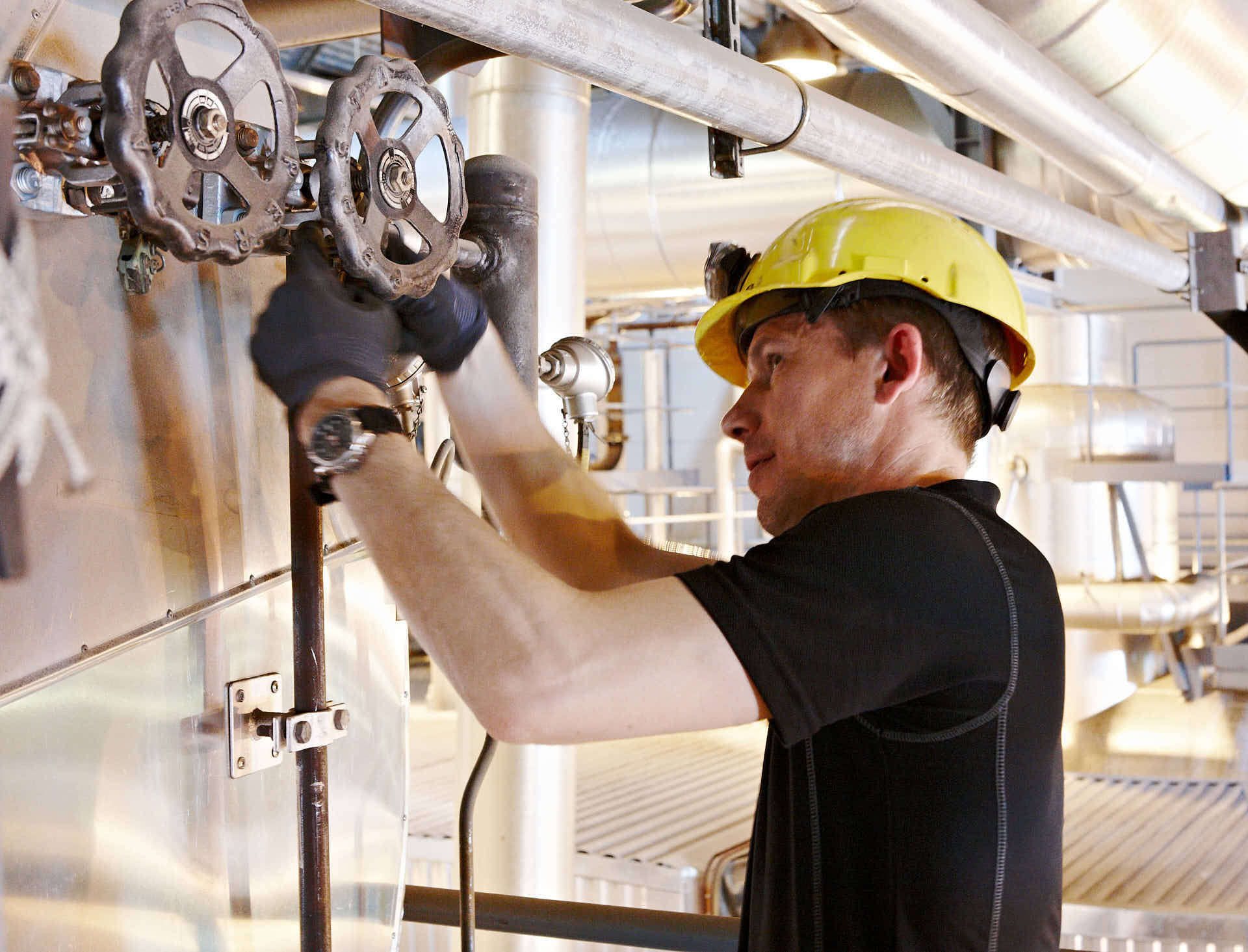 Nicklas Olofsson justerar flödena vid Ena Energis värmeverk som producerar el och fjärrvärme av biobränsle. Luften är het ca 60 grader. Foto av Martin Ekwall.