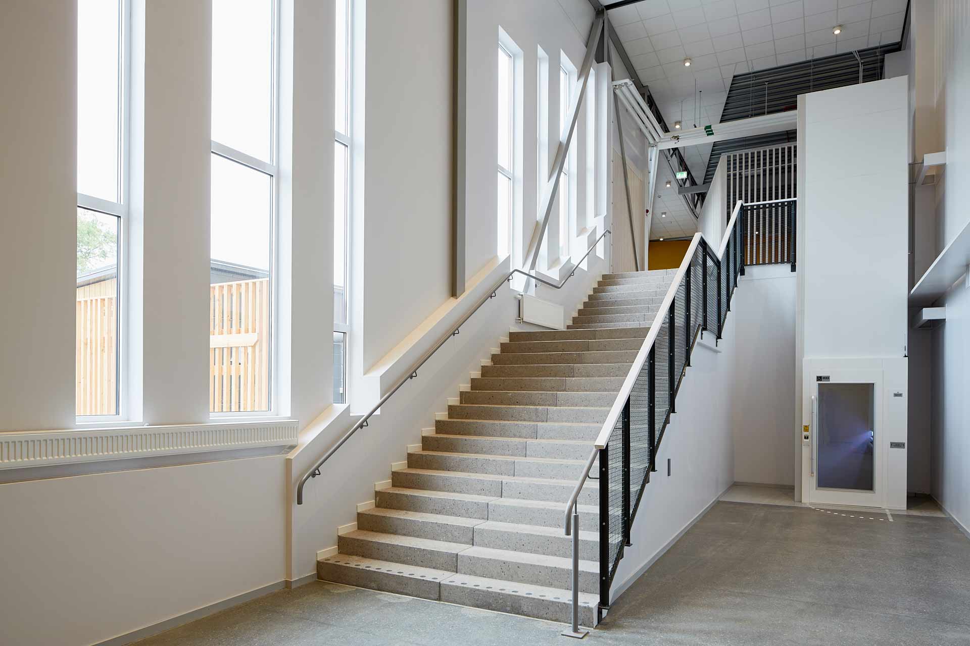 Ekebyhovs sporthall på Ekerö: ljus trappa i entréhall med höga fönster och räcken. Byggd av In3prenör, ritad av Comarc Arkitekter. Foto Martin Ekwall.