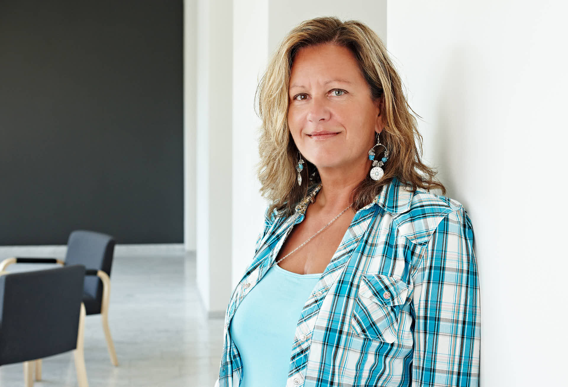 Kvinna i blå- och vitrutig skjorta står mot vit vägg i ljus kontorsmiljö, fotograferad för Svenska Möten kundcase. Foto Martin Ekwall