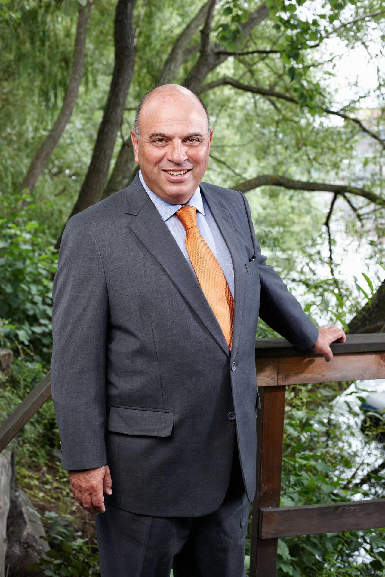 Porträtt av tidigare vice vd Jan Fridman från 3L Systems. Leende i kostym med handen på staket vid träd och brygga. Foto av Martin Ekwall.
