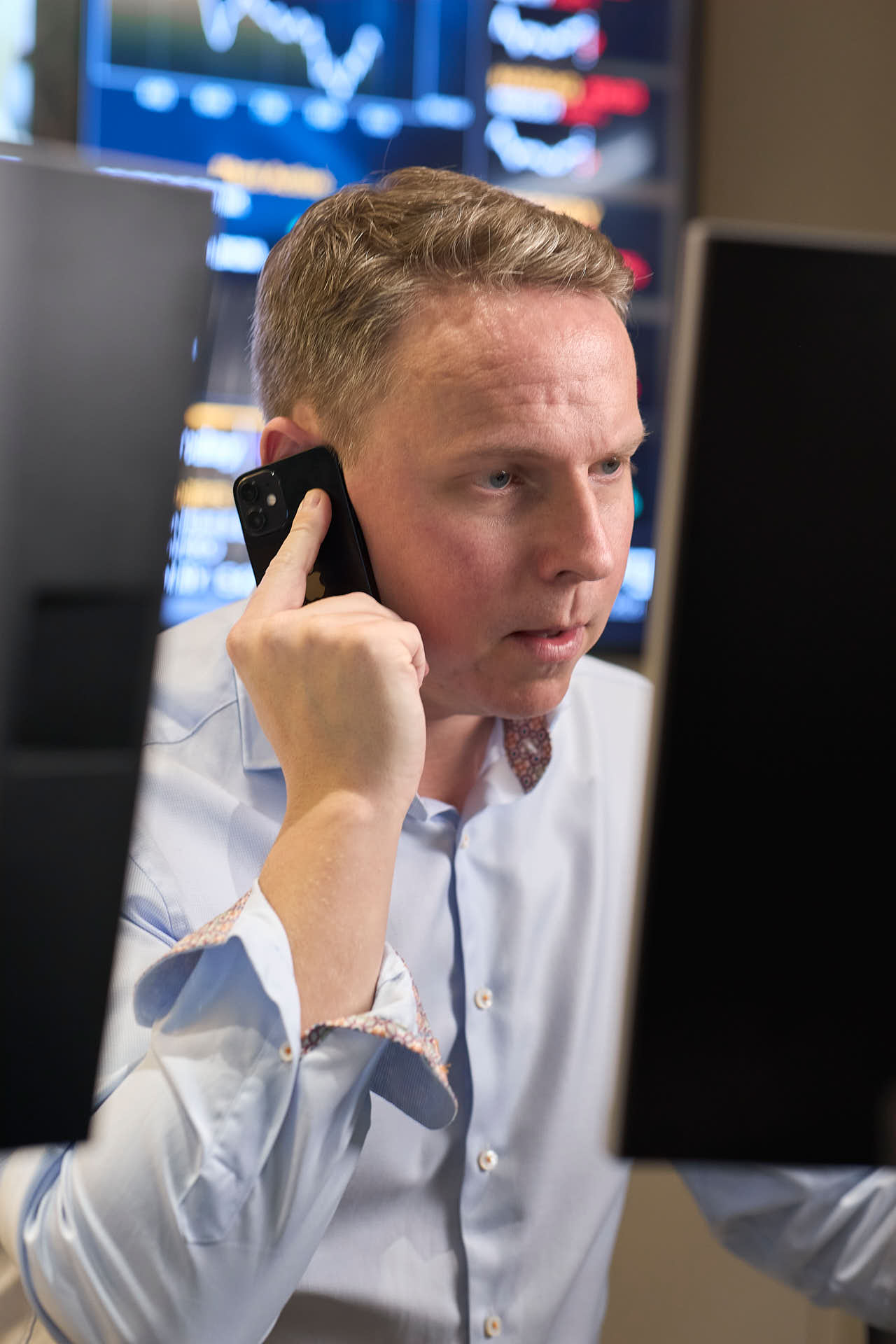 Case Kapitalförvaltning, Andreas Rask tittar på datorskärm talar i telefon, aktieindex i bakgrunden. Foto av Martin Ekwall.