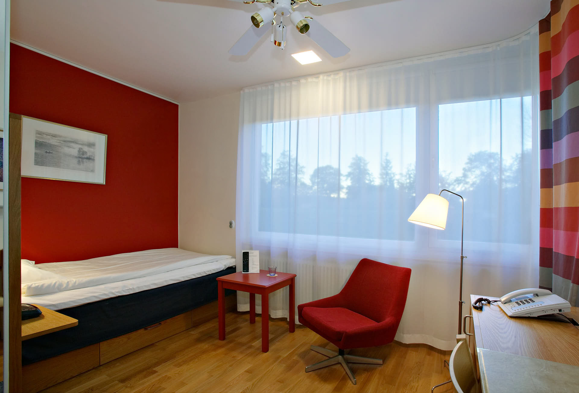 Gällöfsta Herrgård, litet hotellrum enbäddssäng i kvällsljus med fåtölj och skrivbord. Foto Martin Ekwall