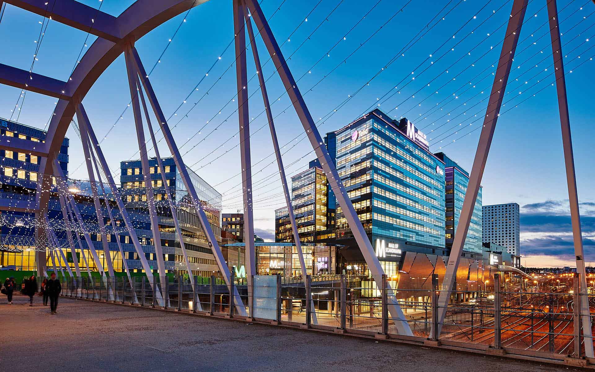 Uppdrag åt Fabege med Teliahuset och SEB i skymning och kvällsljus. Vy från bron till pendeltågstationen, foto Martin Ekwall.