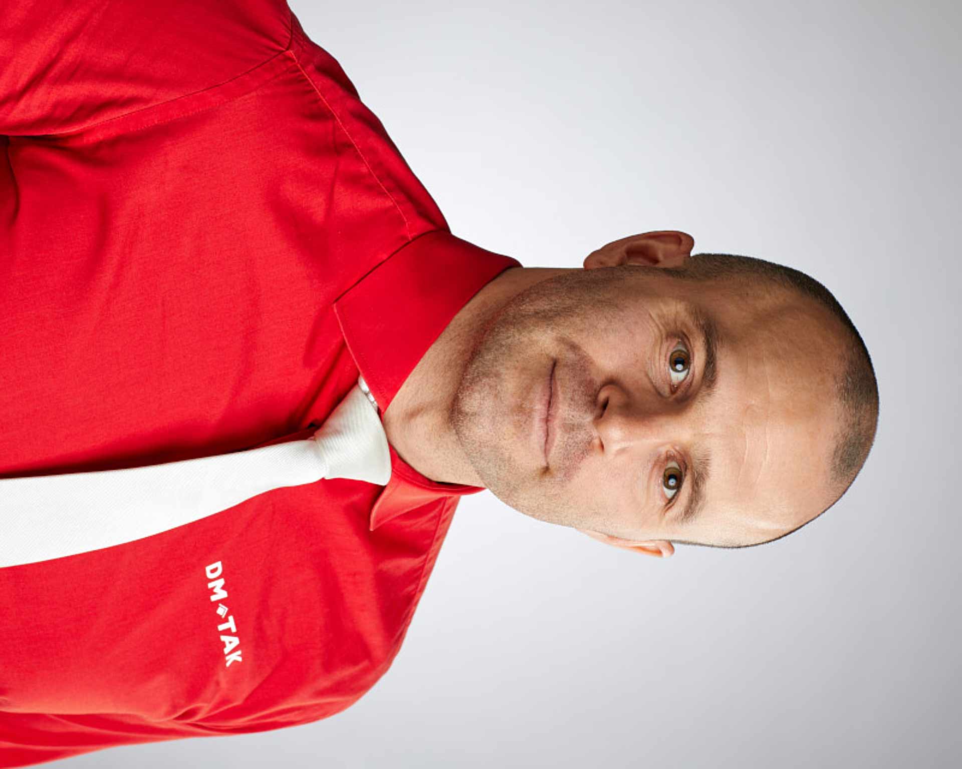 Porträtt av VD David Frykman i röd DM-Tak-skjorta mot ljus bakgrund. Foto Martin Ekwall.