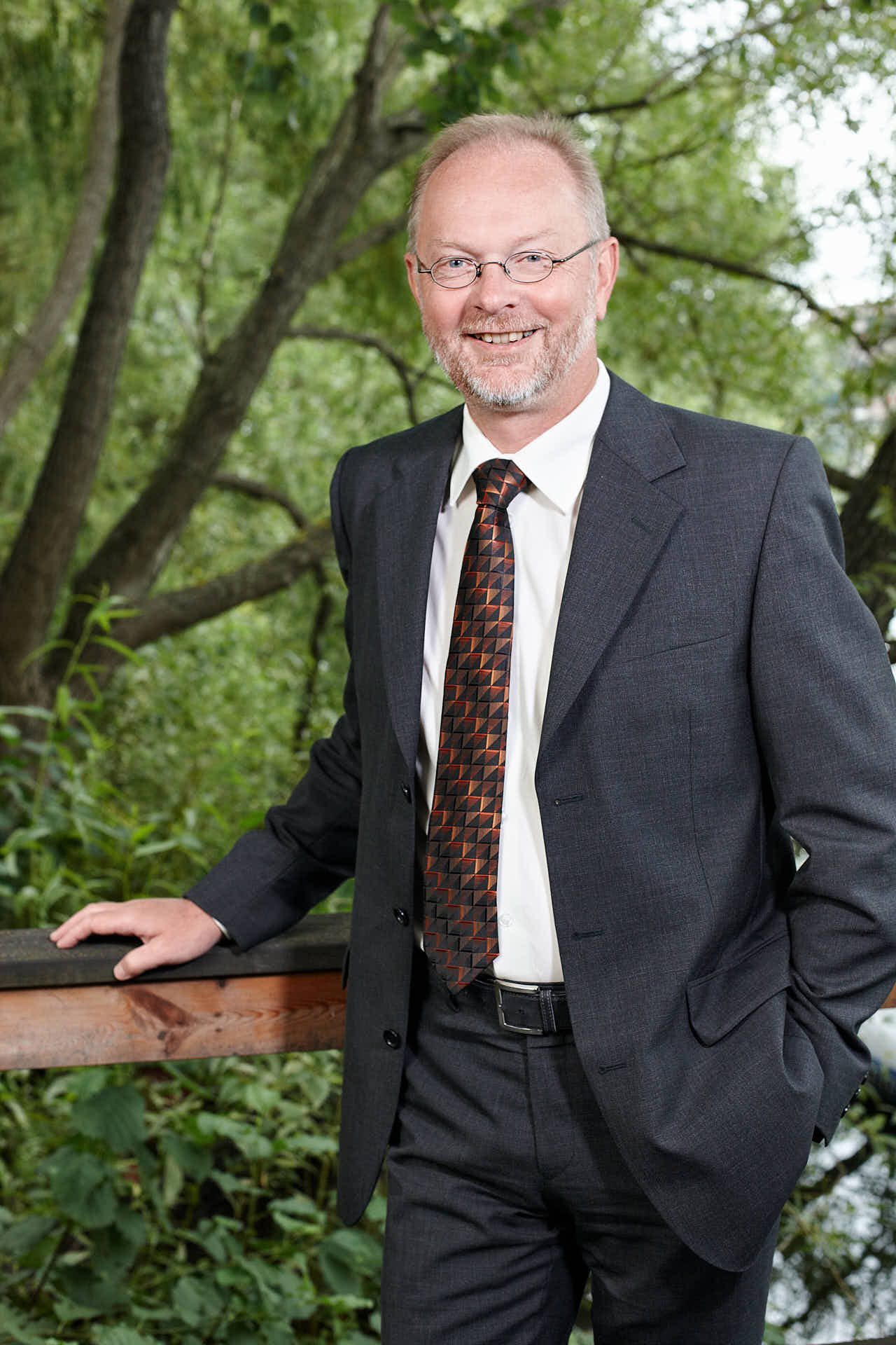Porträtt av tidigare medarbetare Lars Stenlund från 3L Systems. Leende i kostym vid staket och träd. Fotograferat av Martin Ekwall.