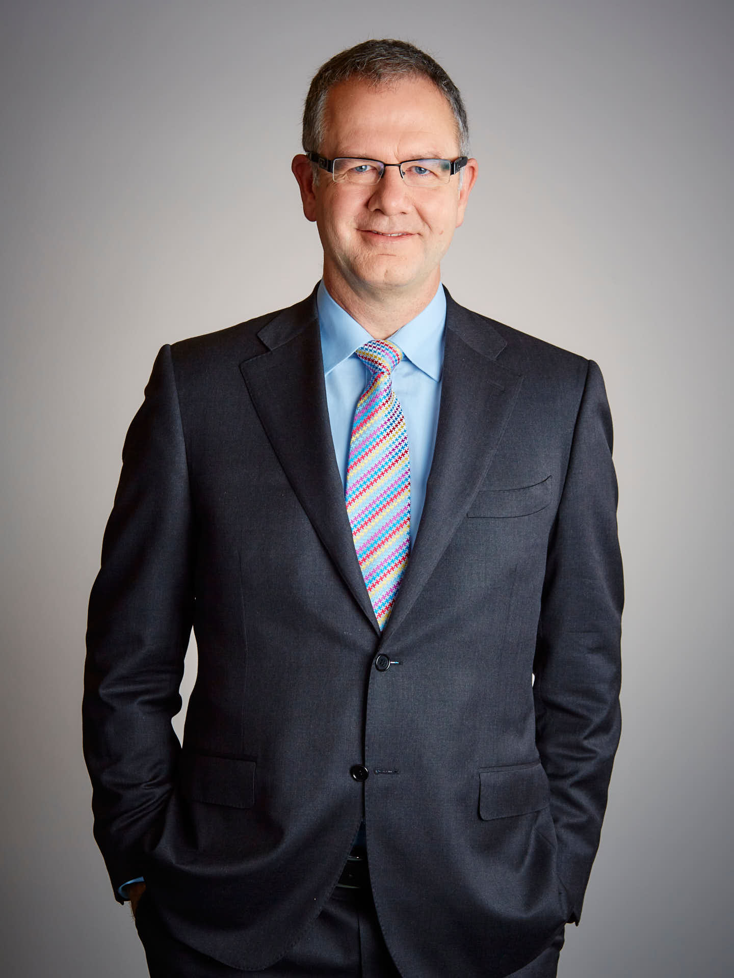 Styrelsemedlem på Ramirent man i mörk kostym och färgglad slips, porträtt i halvfigur avslappnad men ändå pondus i blicken mot grå bakgrund. Foto Martin Ekwall.