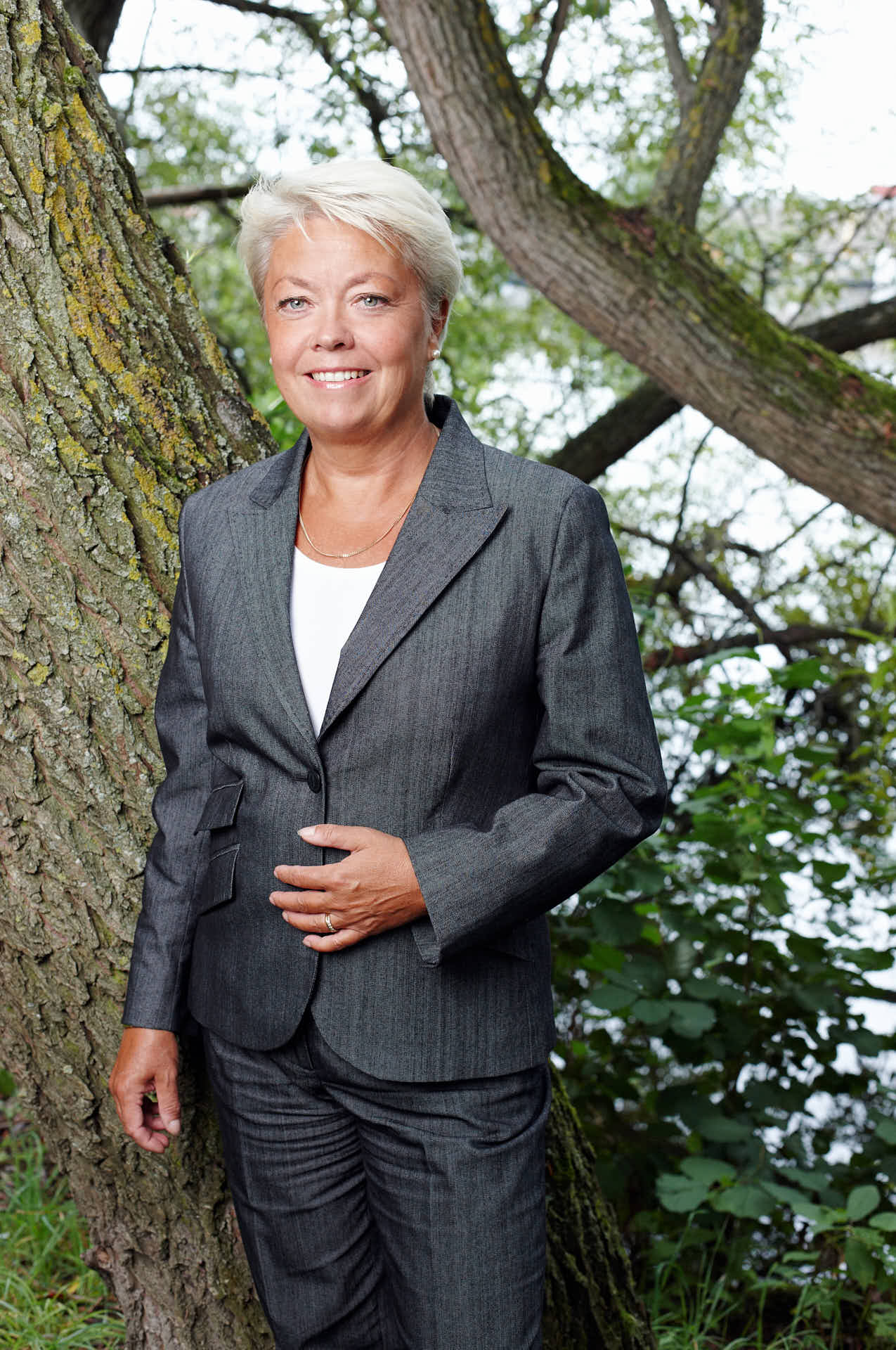 Porträtt av tidigare medarbetare Maria Seifert från 3L Systems. Ena handen på magen framför träd, avslappnat uttryck. Foto av Martin Ekwall.