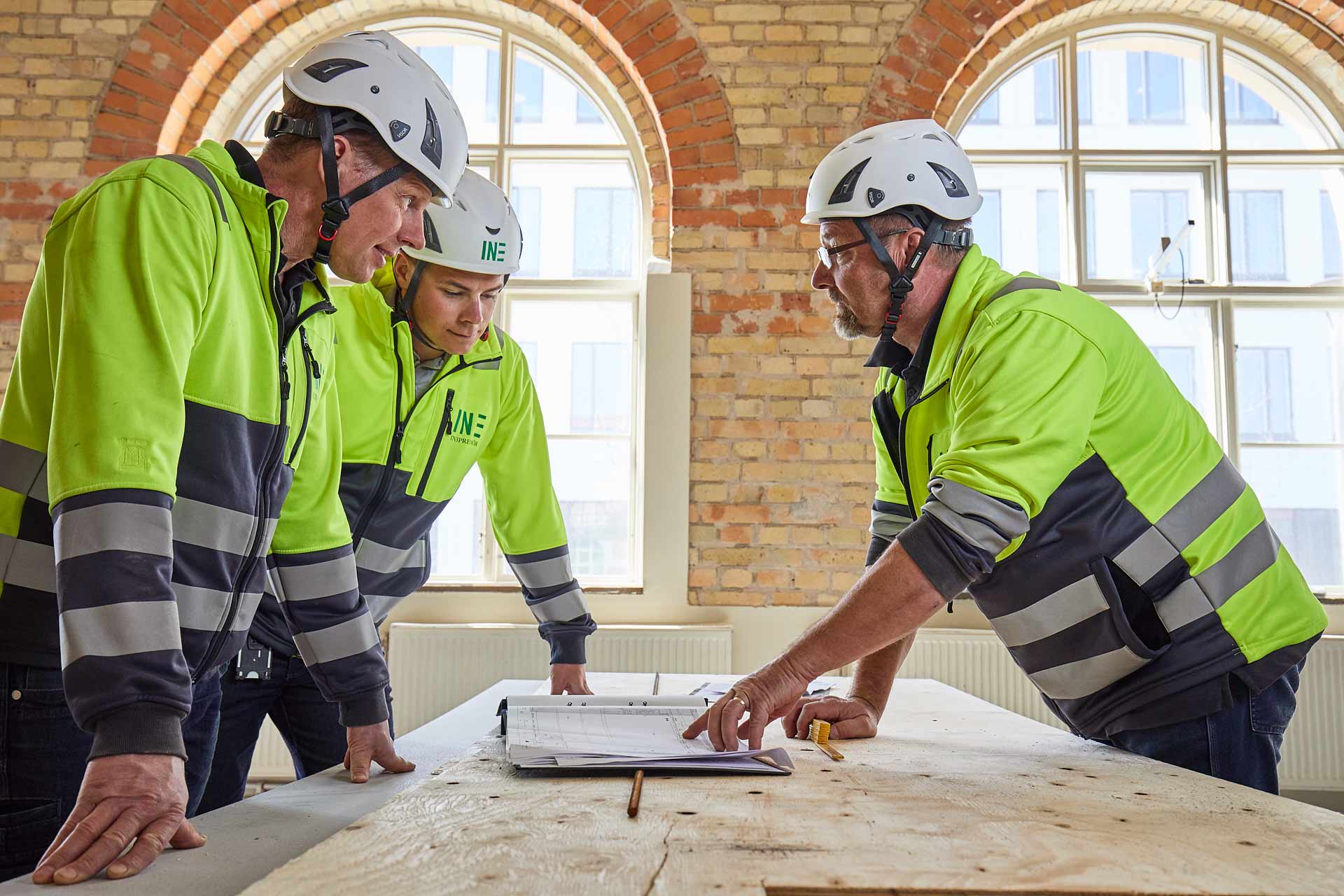 Medarbetare från In3prenör diskuterar ritning vid fönster i byggnad under byggprojektledning. Foto Martin Ekwall.